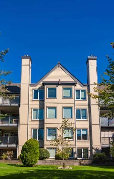 Parlak güneşli bir günde önünde yeşil çimenler olan apartman.
