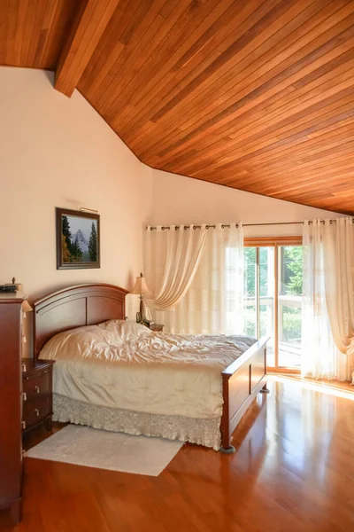 Piękna sypialnia z drewnianym sufitem i światło słoneczne przechodzi przez szklane drzwi. — Zdjęcie stockowe