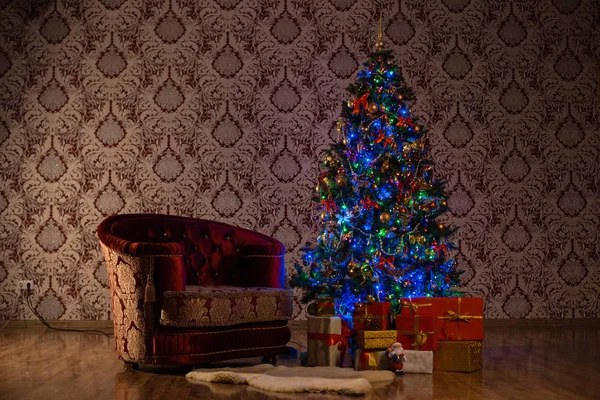 Темная рождественская сцена с зажженной елкой, подарками и креслом — стоковое фото