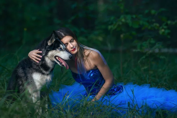 Портрет красивой роскошной гламурной девушки с хаски-собакой, сидящей в синем платье на открытом воздухе в траве — стоковое фото