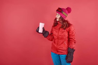 Radyoaktif kayak kıyafetleri ve maske takan stüdyo fotoğrafçısı kadın. Kırmızı arka planda süslemeli duruyor.