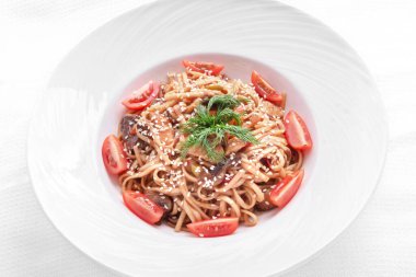 Kiraz domatesli İtalyan makarnası, mantar, susam ve dereotu yuvarlak tabakta. Yukarıdan bak. beyaz üzerine izole