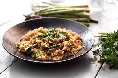 Risotto kuşkonmaz ile. Bir tabakta bir tabak kahverengi pirinç ve kuşkonmaz.
