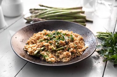 Risotto kuşkonmaz ile. Bir tabakta bir tabak kahverengi pirinç ve kuşkonmaz.