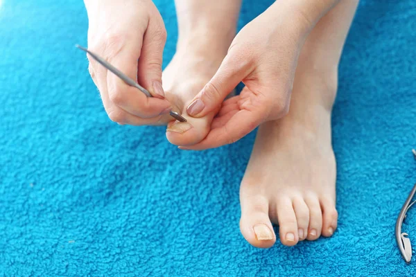 Homemade pedicure, woman cares for the feet, cuticles. The woman is performing a pedicure treatment. Bare feet on a blue towel. composition, real picture without retouching — Stock Image Homemade Pedicure Woman Cares Feet Cuticles Woman Performing Pedicure Treatment Royalty Free Stock Photos