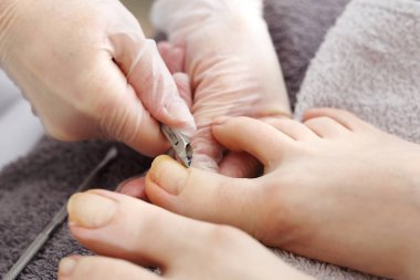 Pedikür, ayak bakımı, güzellik salonunda pedikür sırasında kadın ayakları. Güzellik uzmanı pedikür yaptırıyor. Tedavi sırasında gri bir havlunun üzerinde çıplak ayaklar. Doğal fotoğraf, rötuş yok..