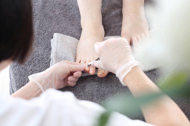 Pedikür, ayak bakımı, güzellik salonunda pedikür sırasında kadın ayakları. Güzellik uzmanı pedikür yaptırıyor. Tedavi sırasında gri bir havlunun üzerinde çıplak ayaklar. Doğal fotoğraf, rötuş yok..