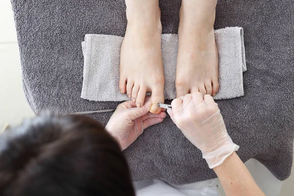 Pedicure, Foot care, female feet during a pedicure at a beauty salon. The beautician performs a pedicure treatment. Bare feet on a gray towel during care treatment. Natural photo no retouching.