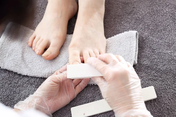Pedicure, nail sawing. Sawing nails, female feet during a pedicure at a beauty salon. The beautician performs a pedicure treatment. Bare feet on a gray towel during care treatment. Natural photo no retouching. — Stock Image Pedicure Nail Sawing Sawing Nails Female Feet Pedicure Beauty Salon Royalty Free Stock Images