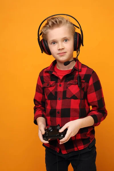 少年はヘッドフォンでコンソールで演奏します 黄色い背景の赤いシャツを着たハンサムな白人の少年水平 真っすぐ — ストック写真
