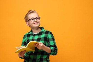 Kitap okuma. Gülümseyen, kitap okuyan mutlu çocuk. Renkli sarı bir arka planda bir çocuğun portresi..