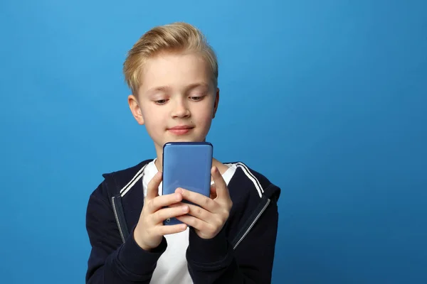 電話で遊べ若い男の子がスマートフォンで遊んでいる 青色の背景に子供の肖像画 表情で表現される感情や感情 — ストック写真