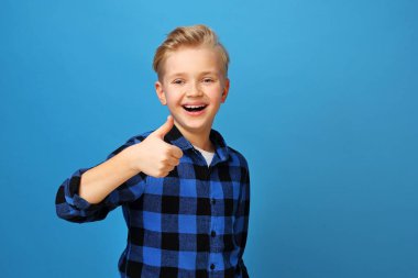 Jest tamam, neşeli çocuk parmaklarını gösteriyor. Mavi arka plandaki mutlu, gülümseyen çocuk duygularını jestlerle ifade eder..