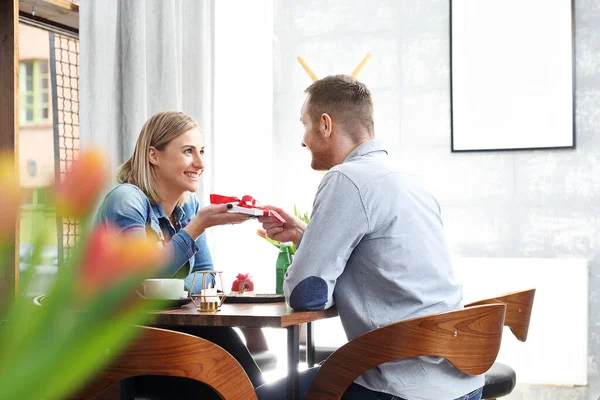 A woman and a man during a social meeting in a cafe. Real life.Giving a gift, birthday, surprise.