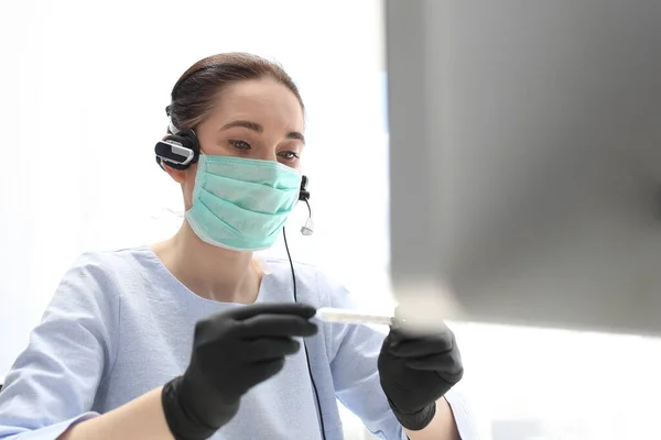 仕事中の病気 外科用マスクの女性がコンピュータ上で動作します 疫病の間の仕事 外科用マスクとヘッドフォンの女性がコンピュータで働いています — ストック写真