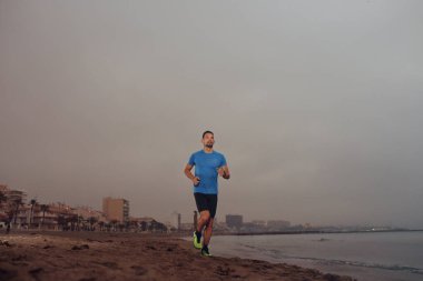 Kumsalda koşmak. Genç atletik çekici bir adam deniz kenarında tek başına koşuyor..