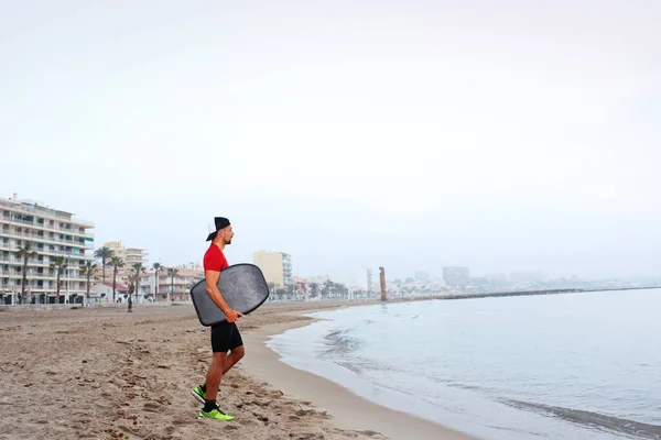 Skimboard, man swims on the board. A man in thermal foam does water sports in the sea.