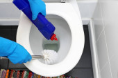 Mosószer-fertőtlenítés. Egy nő fertőtlenítőszerrel tisztítja a WC-t, fertőtleníti a WC ülőkét és a WC-csészét..