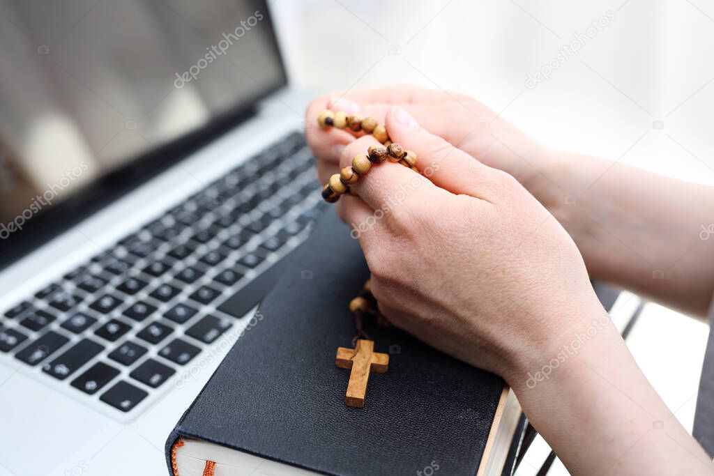 Rosary prayer online, holy mass conducted online. A woman prays on a rosary in front of a computer.