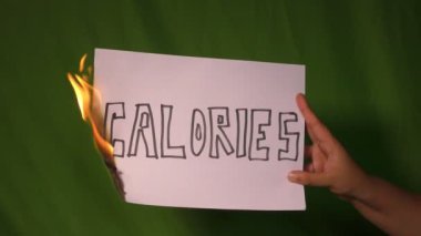 Bir el, üzerinde kalori olan yanan kağıdı yeşil ekranda tutar..