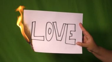 Bir el, arkasında aşk mesajı olan yanan kağıdı yeşil ekranda tutar..