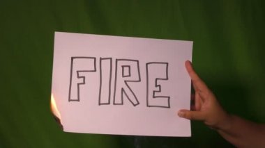 Bir el, arkasında ateş mesajı olan kağıdı yeşil ekranda tutuyor..