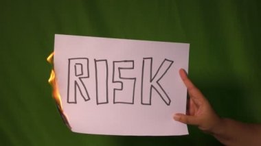 Bir el, yeşil ekranda üzerinde riskli mesaj olan yanan kağıdı tutar..