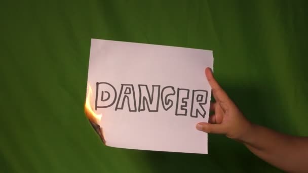 手の後ろの緑の画面に危険性のテキストの単語を持つ燃焼紙を保持します — ストック動画
