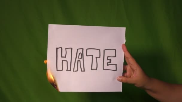 一只手扶着燃烧的纸 上面有仇恨的文字 放在绿色的屏幕后面 — 图库视频影像