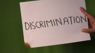 Bir el, üzerinde ayrımcılık yazılı kağıdı yeşil ekranda tutuyor..