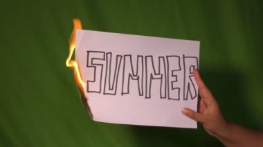 Bir el, yeşil ekranda üzerinde yaz bölücü yazı olan yanan beyaz kağıdı tutuyor..