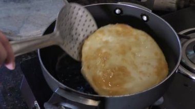 Kaynar yağda bhature kızartır ve elle kaşıkla kenarları çevirir..