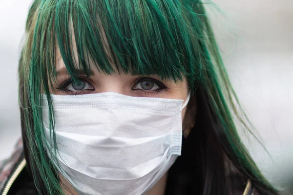 Sokakta maske takmış yeşil saçlı genç bir kız.