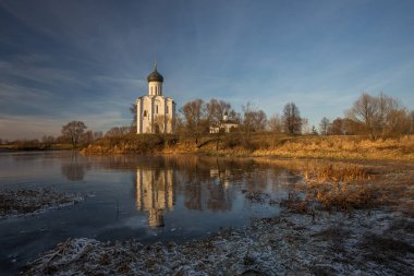 Parlak mavi gökyüzünün arka planında güzel bir tapınak gün batımında buza yansıyan bir gölün kıyısında duruyor.