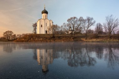 Parlak mavi gökyüzünün arka planında güzel bir tapınak gün batımında buza yansıyan bir gölün kıyısında duruyor.