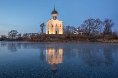 Parlak mavi gökyüzünün arka planında güzel bir tapınak gün batımında buza yansıyan bir gölün kıyısında duruyor.