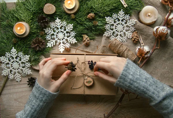 Top view. Table decorated with Christmas decorations (Christmas tree branches, snowflakes, candles, cones). Hands pack, decorate craft Christmas box.