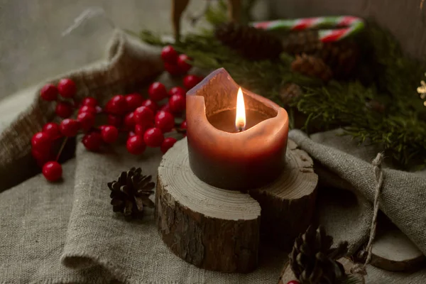 Bir Noel dekoru içinde (kırmızı böğürtlen, karamel, koni) pencereye karşı bir pencere pervazındaki ahşap bir şamdanda durur.