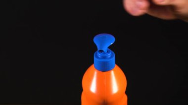 Turuncu deterjan şişesi. Etiketsiz ve isimsiz bir şişe. Elin deterjanı sıkıyor. Bulaşık deterjanı. Ev temizliği.