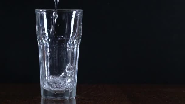 Verre sur fond noir. Verser de l'eau dans un verre. Conteneur transparent. De l'eau pure. Mouvement lent .