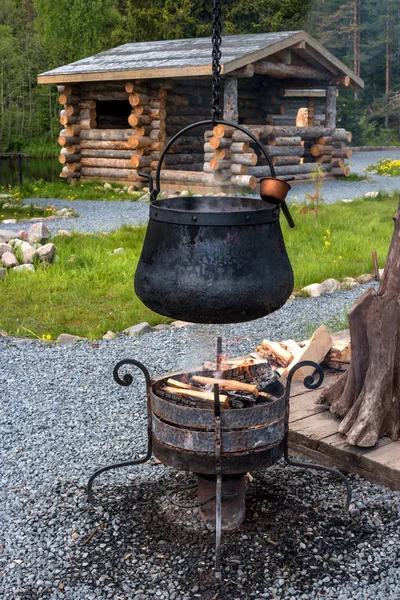 L'eau bout dans le chaudron au-dessus d'un feu ouvert. Le chaudron est noir de suie. En arrière-plan, la maison est faite de grumes . — Photo