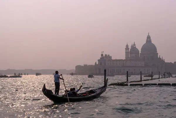 Venice, Italy - October 13, 2017: Gondolier operates a gondola with tourists in the waters of the Canal Grande in the background of the cathedral of Santa Maria della Salute. — Stock Photo, Image