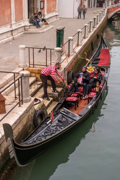 Venezia, 13 ottobre 2017: Gondolier aiuta la rete passeggeri in gondola. La gondola è riccamente decorata con tappeti rossi e ornamenti in oro . — Foto Stock