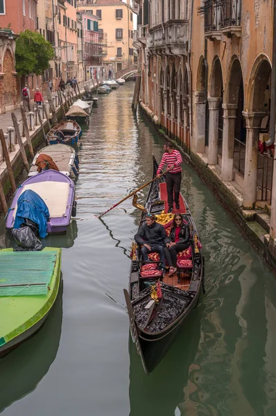 Venice, Italy - October 13, 2017: Tourists sail on a gondola on a narrow canal. The gondola is richly decorated with red carpets and gold ornaments. — Stock Photo, Image