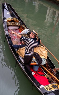 Venice, İtalya - 13 Ekim 2017. Turistler gondol dar bir kanal boyunca yüzme. Gondolcu konumlar için işaret eder. Gondol kırmızı Halılar ve altın süs eşyaları ile süslüdür.