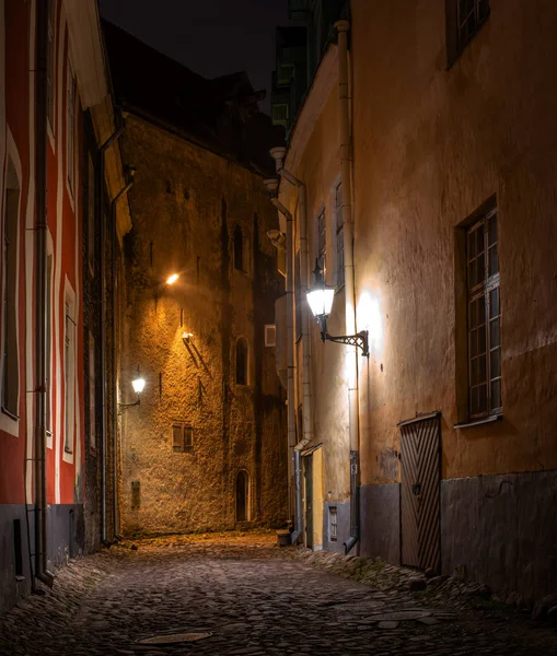 Calle nocturna en el casco antiguo de Tallin, Estonia. Linternas vintage iluminan una calle vacía y empedrado camino —  Fotos de Stock