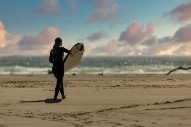 Surfers wearing wetsuits approach the green waters of Mendocino'