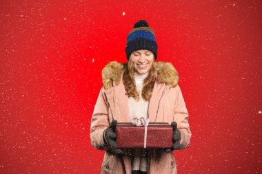 Genç bir kadın elinde bir Noel hediyesi tutuyor ve kar yağıyor.