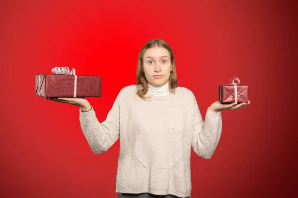 Jeune femme tient deux cadeaux dans sa main et ne peut pas décider pour un — Photo