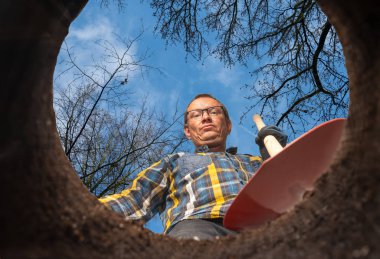 Kürekli bir adam yerde bir delikte duruyor.